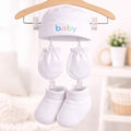 Baby hat and booties set hanging on a wooden hanger with clips against a blurred indoor background.