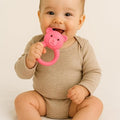 Baby holding a pink teddy bear rattle against a plain background