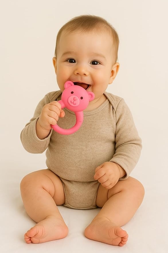 Baby holding a pink teddy bear rattle against a plain background