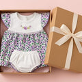 Baby outfit with floral pattern and white bloomers in a gift box on a pink background