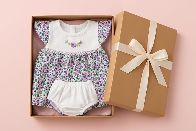 Baby outfit with floral pattern and white bloomers in a gift box on a pink background