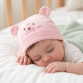 Baby sleeping in a crib wearing a pink bear hat