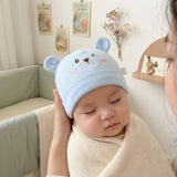 Baby wearing a blue bear hat being held by an adult in a cozy room.