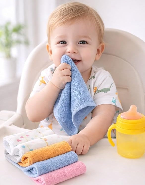 Child in a high chair holding a blue towel with colorful towels and a yellow sippy cup on a table.