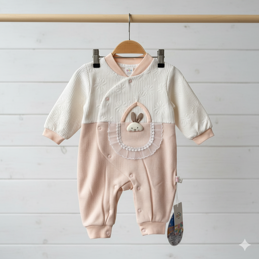 Baby romper with bunny design hanging on a wooden rod against a light wooden panel background