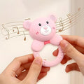 Pink bear-shaped teething ring held by hands with musical notes in the background