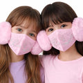 Two children wearing pink face masks with pom-pom attachments on a white background