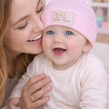 Woman holding a baby wearing a pink bear hat indoors
