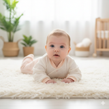 Baby lying on a fluffy rug in a bright, minimalistic room with plants and a crib.