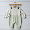 Baby romper with ribbed sweater top and plain bottom on a wooden hanger against a light wooden floor.