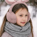 Child wearing pink bunny ear headband and gray scarf in snowy setting